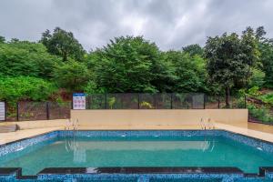 a swimming pool in a backyard with a fence and trees at SaffronStays Riverdale - 4BR pool villa in Lavasa with gazebo, Indonesian artwork, and cricket pitch in Pune