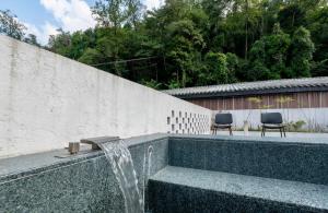 a fountain with two chairs sitting next to a wall at 峨眉山和院一溪清音酒店 in Emeishan City