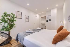a white bedroom with two beds and a plant at Deustown Apartamentos in Bilbao