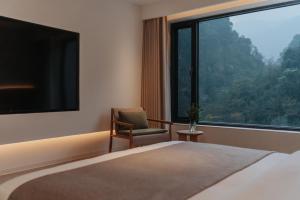 a bedroom with a bed and a chair and a large window at 峨眉山和院一溪清音酒店 in Emeishan City