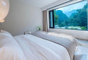 a bedroom with a white bed and a large window at 峨眉山和院一溪清音酒店 in Emeishan City