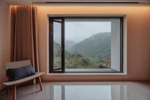 a room with a window with a chair and a view at 峨眉山和院一溪清音酒店 in Emeishan City