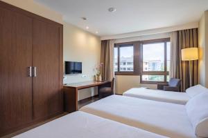 a hotel room with two beds and a desk with a television at Hotel Coia de Vigo in Vigo