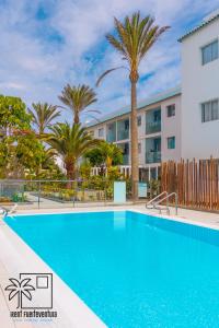a swimming pool in front of a building with palm trees at Hola Jag Corralejo Center iRent Fuerteventura in Corralejo