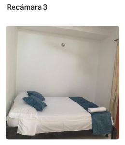 a bedroom with a bed with white sheets and blue pillows at apartamento dúplex con piscina en el Rodadero in Rodadero +3 photos