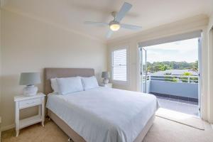 a white bedroom with a bed and a balcony at Sandcastles 4 -8 Ala Moana Way in Fingal Bay +32 photos