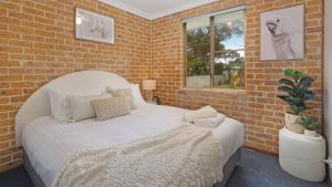 a bedroom with a white bed and a brick wall at Jervis Joy in Callala Beach