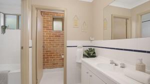 a bathroom with a white sink and a brick wall at Jervis Joy in Callala Beach
