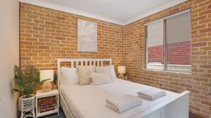 a bedroom with a white bed with a brick wall at Jervis Joy in Callala Beach