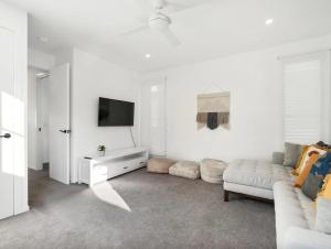 a white living room with a couch and a tv at Cylinders Coastal Deluxe in Kingscliff