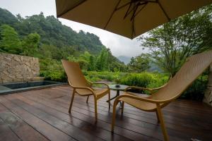 two chairs and a table with an umbrella on a wooden deck at 峨眉山和院一溪清音酒店 in Emeishan City