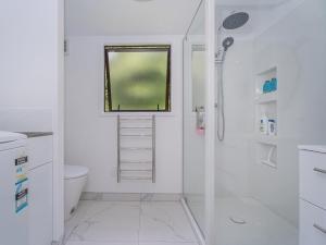 a white bathroom with a shower and a window at Rewa Rewa Retreat - Tairua Holiday Home in Tairua +13 photos