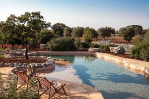 a swimming pool with two chairs in a garden at Trulli di Monte Reale by BarbarHouse in Cisternino