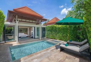 a swimming pool with an umbrella next to a house at Banyan Tree Phuket in Bang Tao Beach