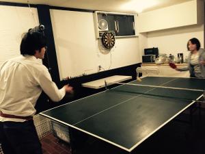 a man and a woman standing next to a ping pong table at Bacchus Kofu Guesthouse in Kofu