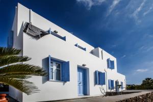 a white building with blue windows and a palm tree at Astarti Apartments in Livadi