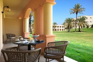 a table and chairs on a porch with palm trees at Almar Timi Ama Resort & Spa in Villasimius