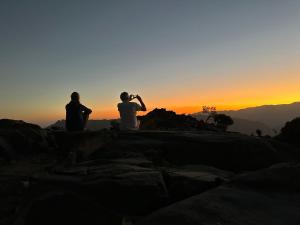 three people sitting on a mountain watching the sunset at Panorama Guest House Jabal Shams in Sa‘ab Banī Khamīs