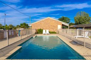 a swimming pool with two chairs and a fence at All Travellers Motor Inn in Coonabarabran