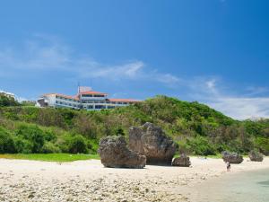 a beach with rocks and a building in the background at Hotel Hamahigashima Resort in Uruma