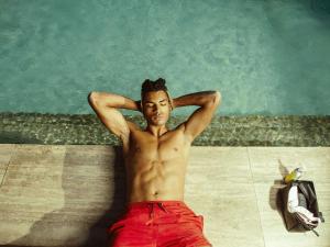 a shirtless man sitting next to a swimming pool at Number 11 St Julian's Malta - Handwritten Collection in St. Julianʼs