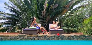 deux femmes assises sur des chaises devant une piscine dans l'établissement La VILLA ANKARENA Dans un domaine forestier tropical, PROPRIÉTÉ ENTIÈRE avec PISCINE PRIVEE, Wifi, TV Plage à 5 minutes à pieds, sur l'île Sainte-Marie 119 autres photos