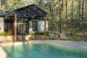 a swimming pool with two chairs and a house at Pokolbin Cottages in Pokolbin
