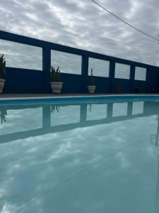 a swimming pool with a blue building and plants at PÉ NA AREIA Apto Manfron in Itapoa
