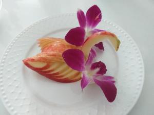 a white plate with a piece of fruit and purple flowers at Baanthanthip in Khon Kaen