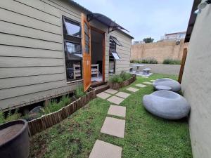 a backyard with a house and some grass and rocks at Petite Cottage Plett in Plettenberg Bay