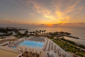 a view of the pool and the ocean at sunset at Queens Bay Hotel in Paphos