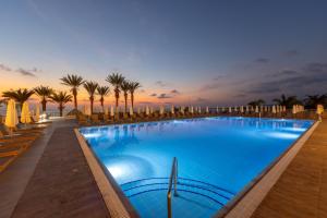a large swimming pool with palm trees and umbrellas at Queens Bay Hotel in Paphos