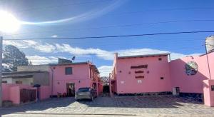 a group of pink buildings with a car parked in a street at Virgen Del Valle Alojamiento in Tafí del Valle