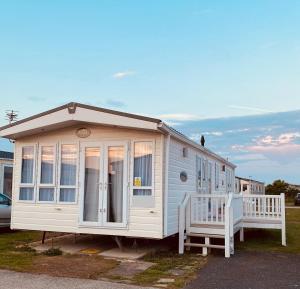 a white house with a porch and two benches at Privately Owned 2-bedroom Caravan at Camber Sands, 1 sofa bed, Private Parking, NO SMOKING NO PETS in Camber
