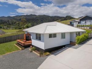 a white house with a fence and mountains in the background at Greenhills Charmer - Coromandel Town Holiday Home in Coromandel Town