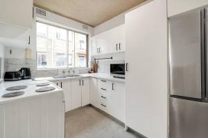 Una cocina con gabinetes blancos y un refrigerador de acero inoxidable. en The 2 Bedroom Hurstville Haven, en Sídney 5 fotos más