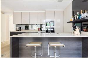 eine Küche mit weißen Schränken und einer Theke mit Stühlen in der Unterkunft Home Sweet Hampstead Heath in London