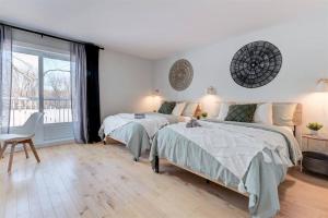a white bedroom with two beds and a chair at Cozy Riverside Cottage Escape with SPA, Pool Table and Dock Access in Rigaud