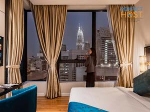 una mujer parada en una habitación de hotel mirando por la ventana en Pavilion Ceylon Hill Suites, Bukit Bintang by Perfect Host, en Kuala Lumpur