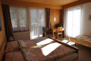 a bedroom with two beds and a desk and windows at Hotel Bellary in Grindelwald
