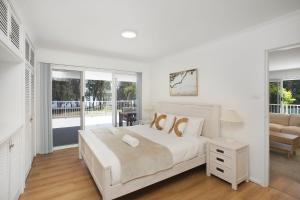 a white bedroom with a large bed and a balcony at Sanctuary Bliss in Sanctuary Point