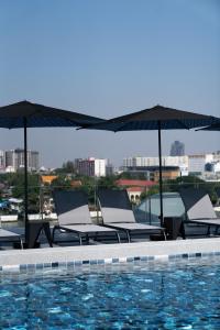 eine Gruppe von Stühlen und Sonnenschirmen neben einem Pool in der Unterkunft The StandardX, Bangkok Phra Arthit in Bangkok