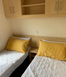 6 BERTH DELUXE PG159 GOLDEN PALM CHAPEL St LEONARDS في شابيل سانت ليوناردز: سريرين في غرفة صغيرة مع وسائد صفراء