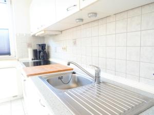 - une cuisine avec un évier en acier inoxydable et du carrelage blanc dans l'établissement Ferienwohnungen Meerfarbig Zingst - HAUSTIERFREI -Terrasse mit Strandkorb oder Balkon - E-Ladesäule - Parkplatz - WLAN - Fahrradschuppen - Waschtrockner - ruhig und zentral - Nichtraucher, à Zingst 109 autres photos