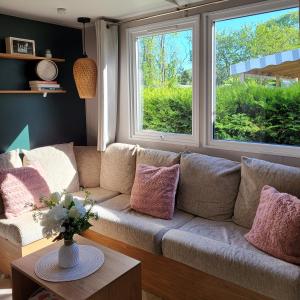 a living room with a couch and two windows at Mobil home gamme luxe 6 personnes camping 5 étoiles in Saint-Georges-dʼOléron