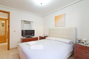 a white bedroom with a bed and a tv at Global Properties, Apartamento muy cerca de la playa de Puerto de Sagunto in Puerto de Sagunto