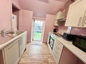 a kitchen with pink walls and white cabinets and a sink at Luxury 3 bed, 6 person, spacious rural apartment in Cwm-brân