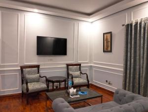 a living room with two chairs and a tv on the wall at Riviera Courtyard Guest House Islamabad in Islamabad