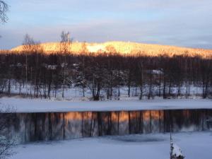 una puesta de sol invernal sobre un lago con una montaña en el fondo en Lottas Rum, en Smedjebacken