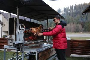 a man in a red jacket cooking meat on a grill at La Ancuța-n Bucovina in Gura Humorului